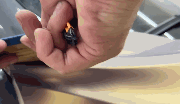A hand using a small tool to precisely trim excess vinyl wrap along the edge of a surface, ensuring a neat application