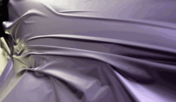 Close-up of a smooth, stretched sheet of glossy purple vinyl wrap being applied, showcasing its texture and flexibility