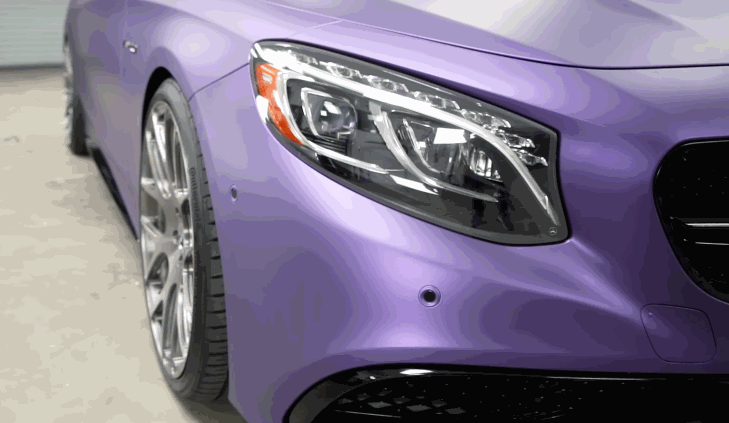 The front of a luxury car wrapped in a matte purple finish, highlighting the headlight and sleek contours of the vehicle