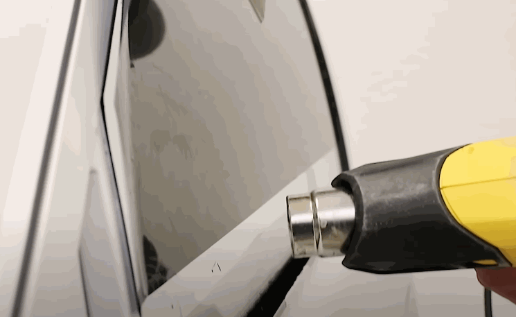 Close-up of a heat gun used on the edge of a car window, activating adhesive for a seamless tint finish.