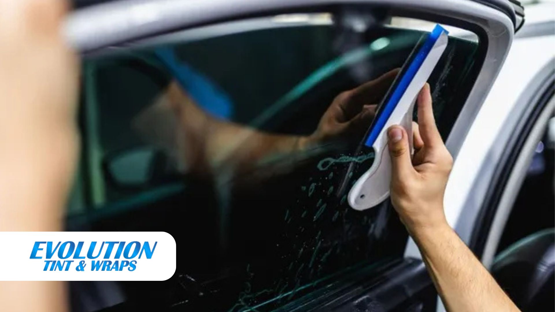 A professional uses a squeegee to smooth out window tint film during an automotive tint installation at Evolution Tint & Wraps
