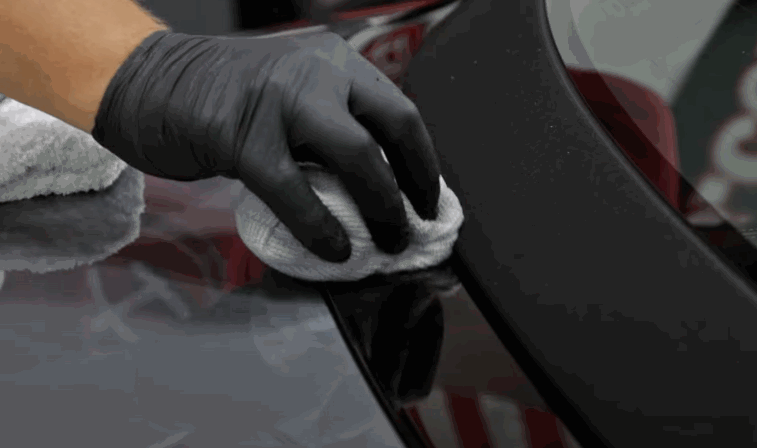 A black-gloved hand uses a white microfiber towel to gently wipe down the car’s polished surface.