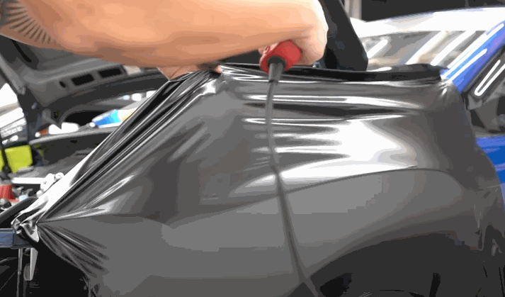 A technician uses a heat gun to stretch and set glossy vinyl wraps over a vehicle’s body panel, eliminating air pockets and wrinkles.