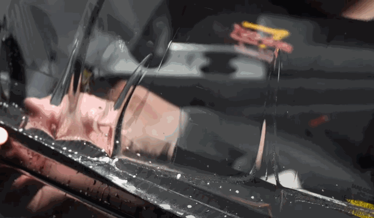 Technician carefully aligning and applying clear tint film onto a car door window, with reflections visible on the glass.