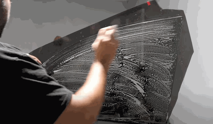 A person cleaning a large piece of auto glass with soap and water before applying window tint film.