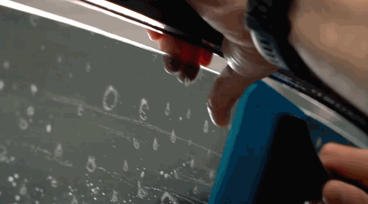 Close-up of a person using a squeegee tool to smooth window tint film onto a wet car window.