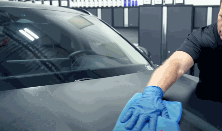 Auto detailing technician in gloves wiping the hood of a car with a microfiber towel inside a professional garage.