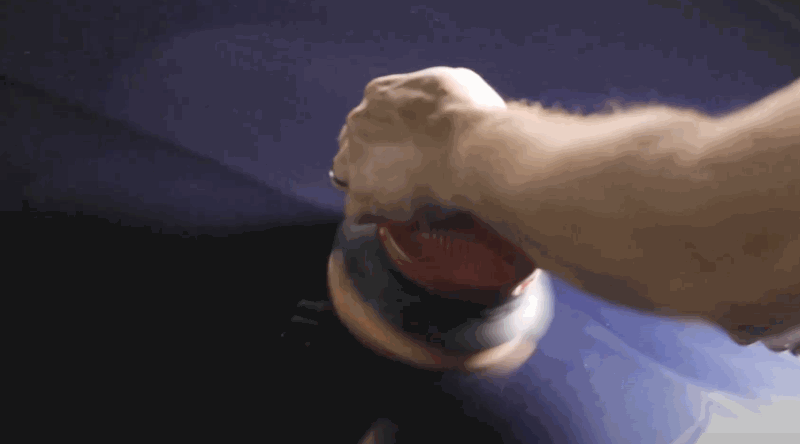 A detailer using an orbital buffer to polish a dark blue car panel, creating a smooth, reflective surface.