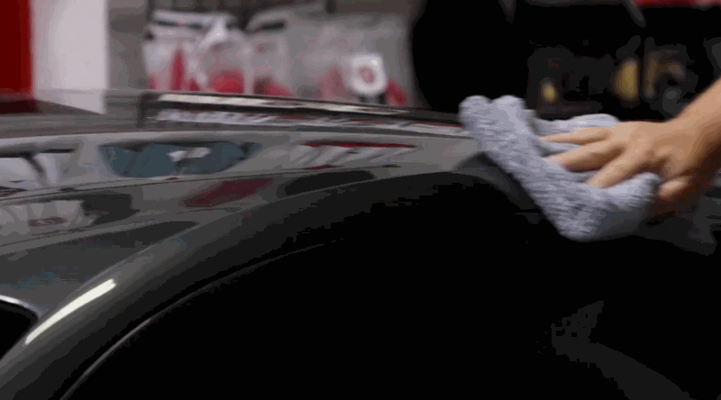 Person buffing the roof of a shiny black car with a soft gray microfiber towel in a detailing shop.