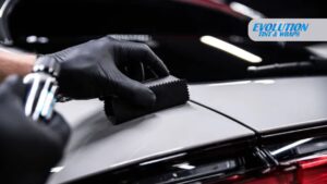 Close-up of a detailer wearing black gloves applying ceramic coating to a white car surface using a foam applicator pad.
