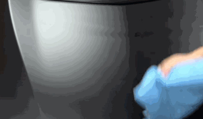 Close-up of a gloved hand wiping down a metallic car panel with a blue microfiber cloth for surface cleaning.