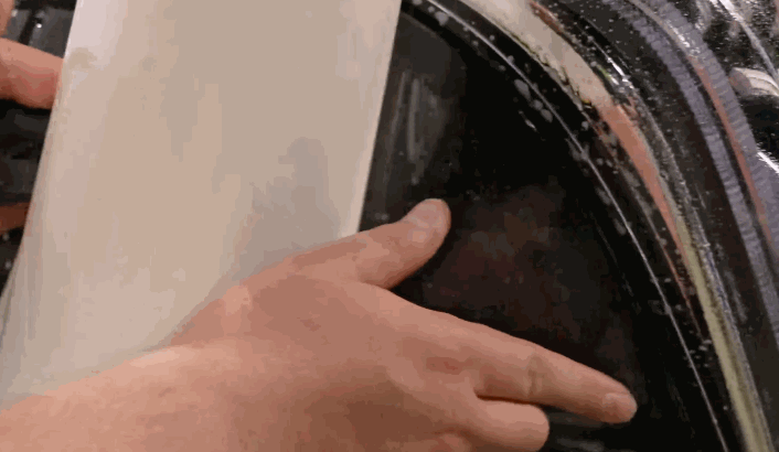 Close-up of hands aligning and pressing paint protection film onto a black car’s headlight.