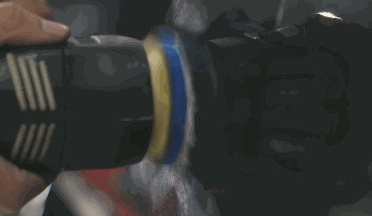 A close-up of a handheld buffer polishing a car's surface, with compound being worked into the paint to restore shine and remove imperfections.