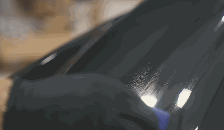 A gloved hand applies ceramic coating to a glossy black car panel using a soft applicator, creating smooth streaks as the liquid is spread evenly.